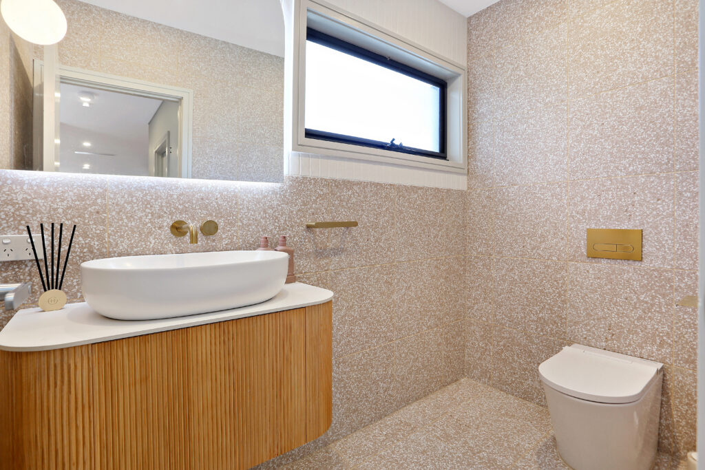 Finished bathroom with a walk-in shower behind a glass sliding screen, toilet and brushed brass tapware